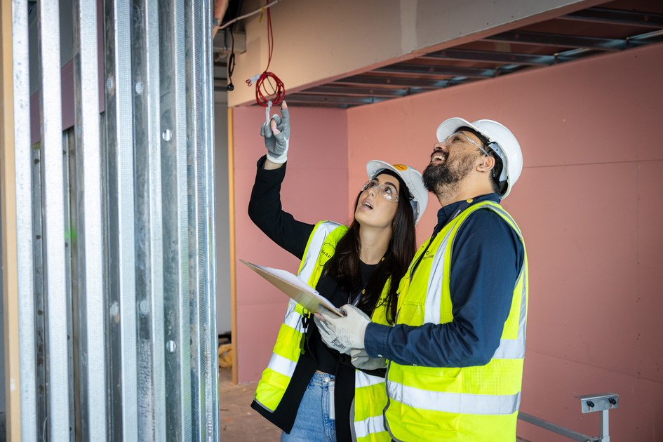 Female and male construction workers collaborating on-site, wearing safety gear and discussing plans